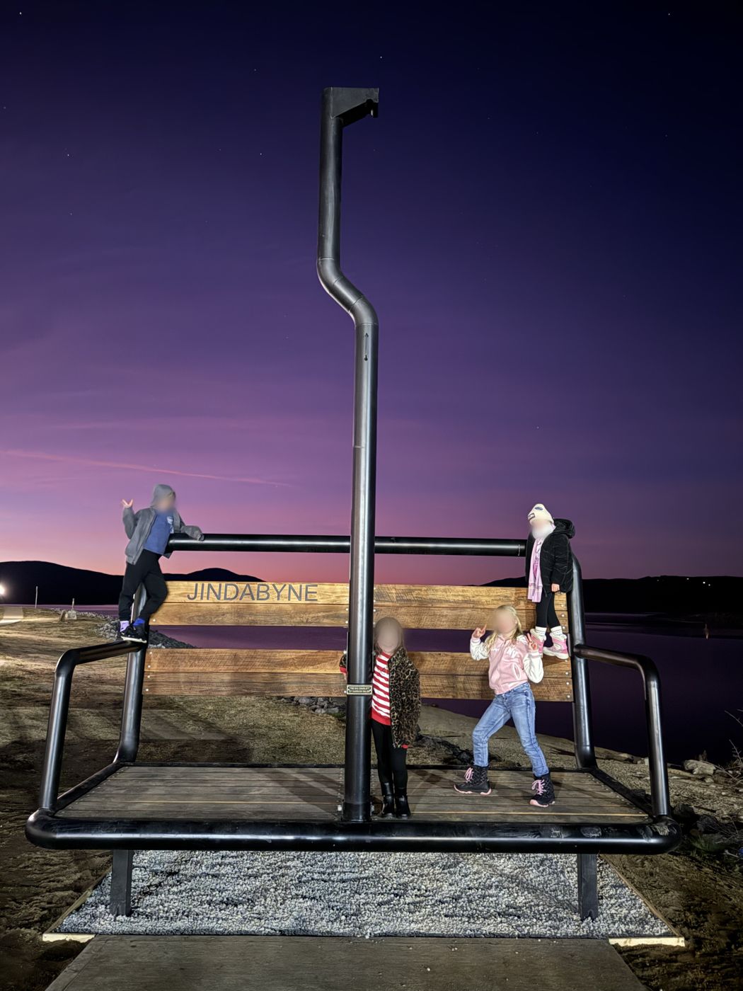 Kids posing on the Big Chairlift sculpture by Lake Jindabyne at dusk