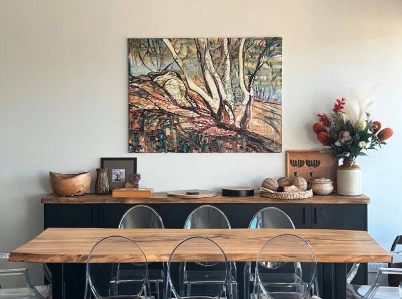 Live-edge dining table and sideboard beneath a large gum tree painting