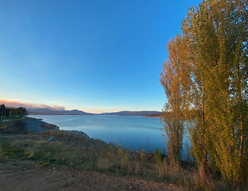 Lake Jindabyne at golden hour, with autumn poplars on the foreshore and the hills beyond
