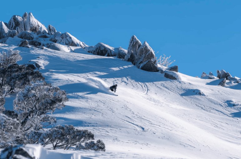 Snowboarder carving through fresh snow below frosted granite tors on a clear blue day